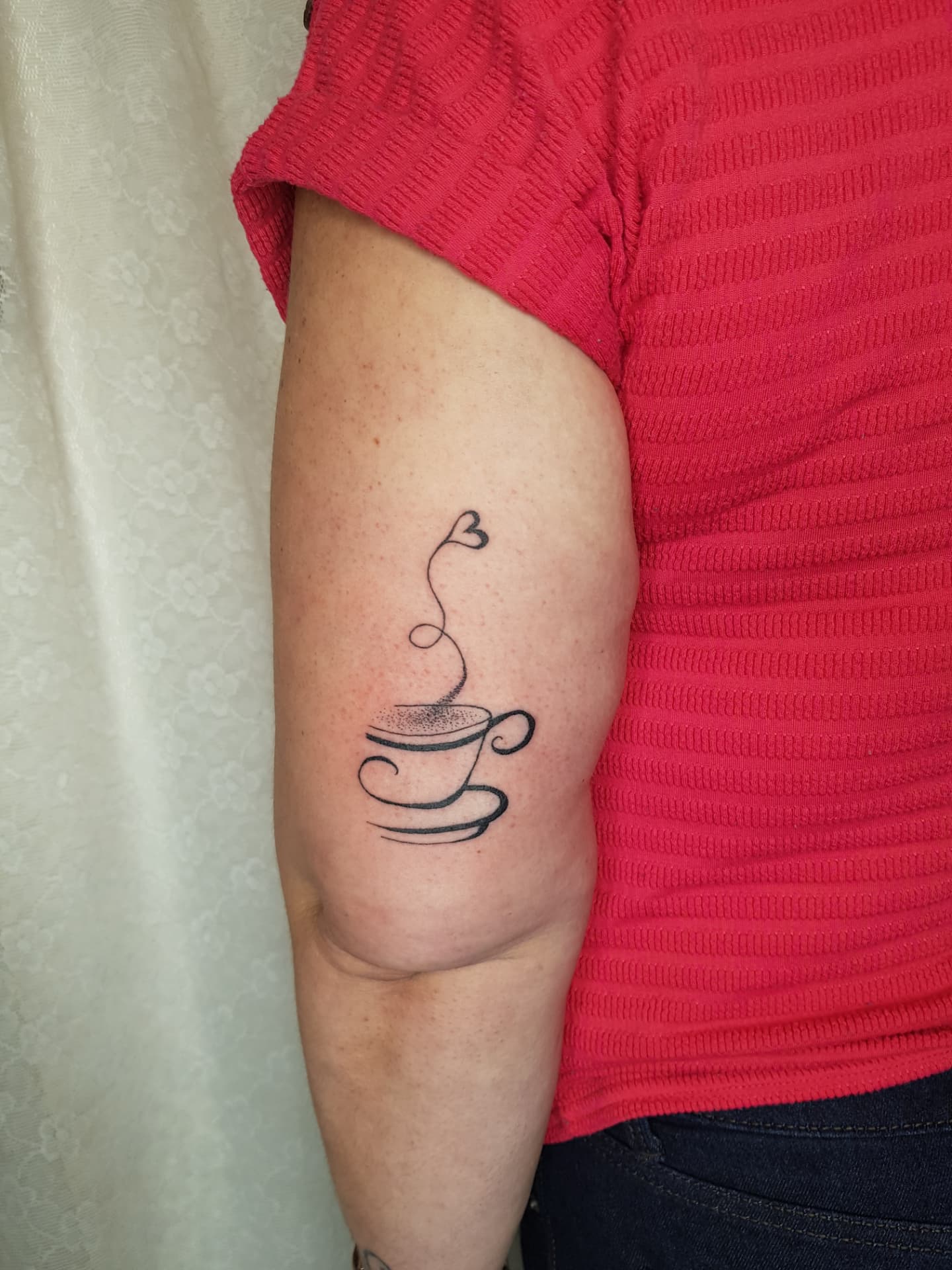 Fine-line teacup with heart-shaped steam tattoo on upper arm