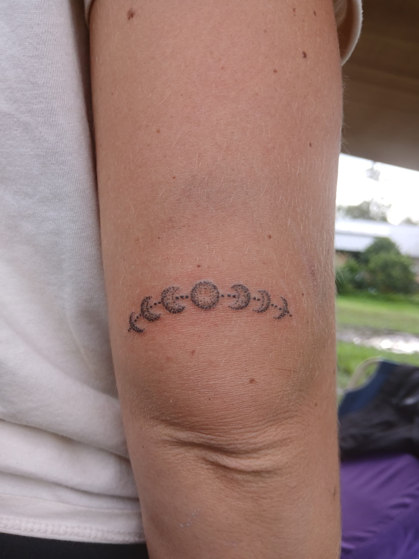 Moon phases hand-poke tattoo above the elbow