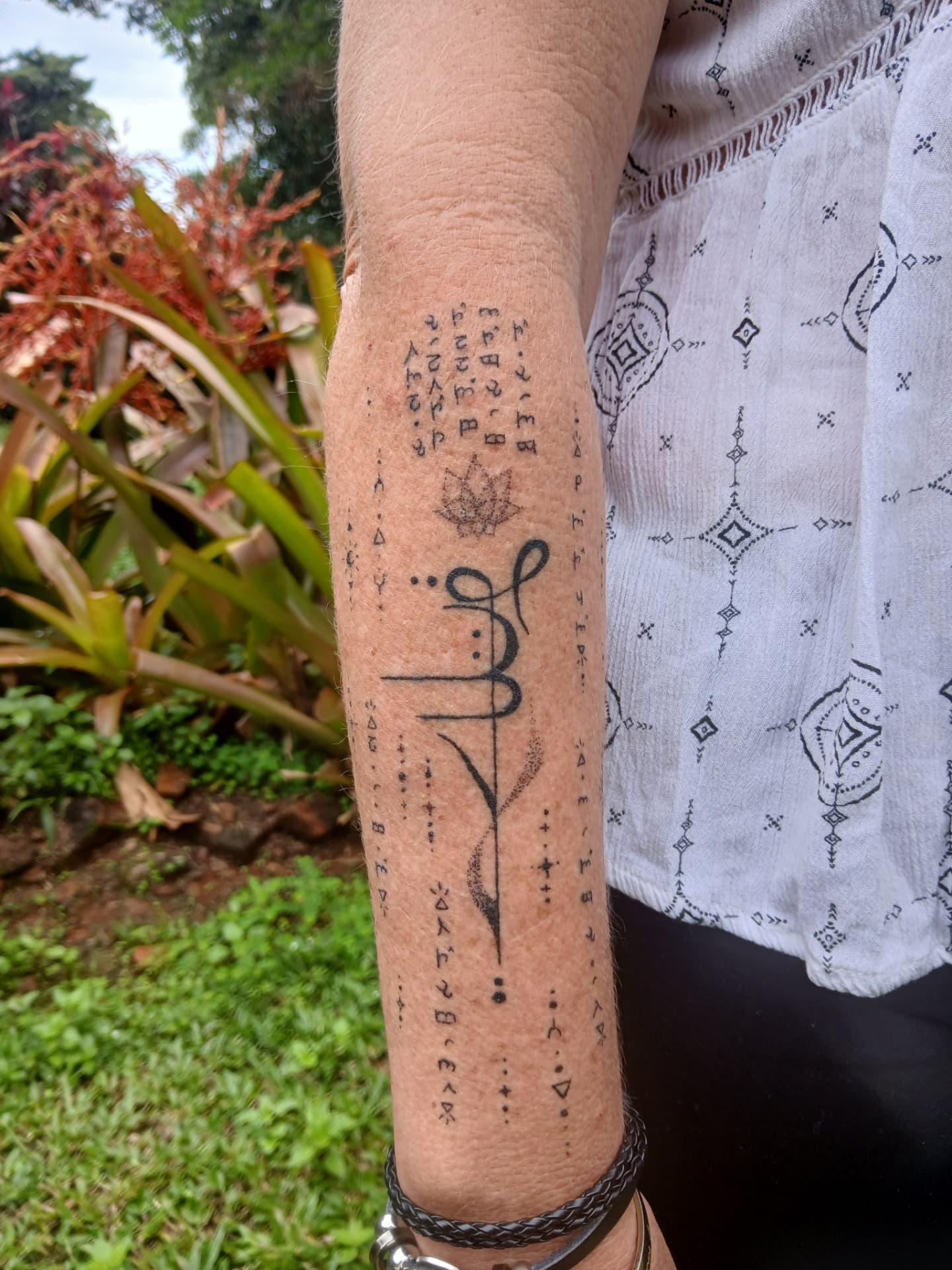 Lotus and symbolic script sleeve tattoo on forearm