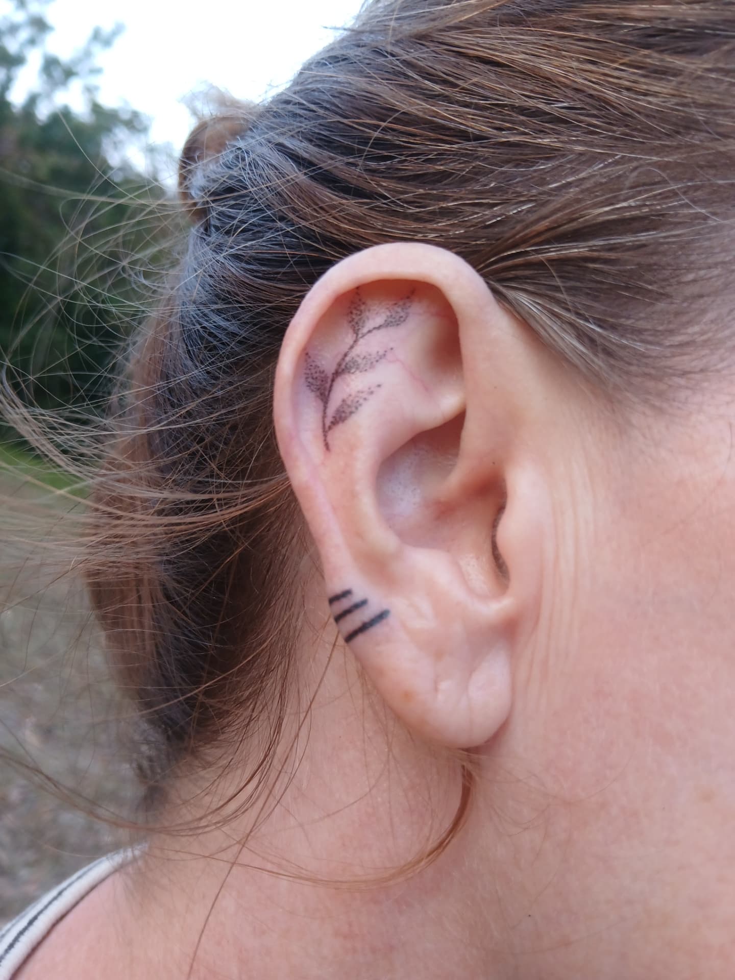 Delicate botanical ear tattoo with fine-line bands